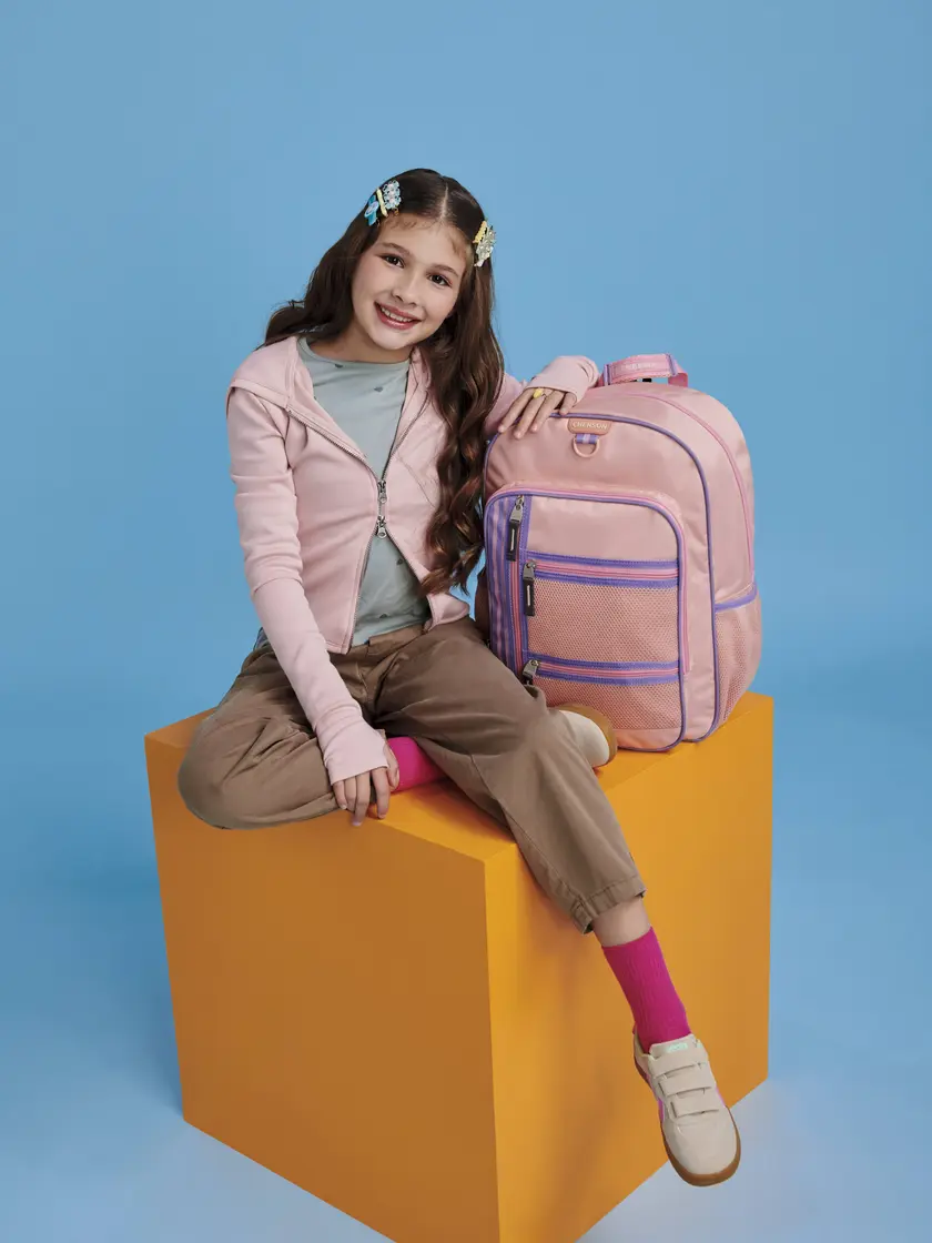 Niña sentada junto a una mochila escolar Chenson rosa con lapicera a juego