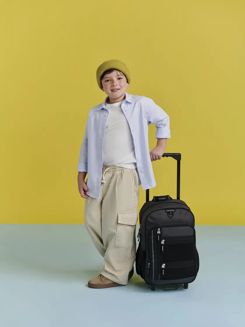 Niño de pie junto a una mochila Chenson con ruedas y asa telescópica